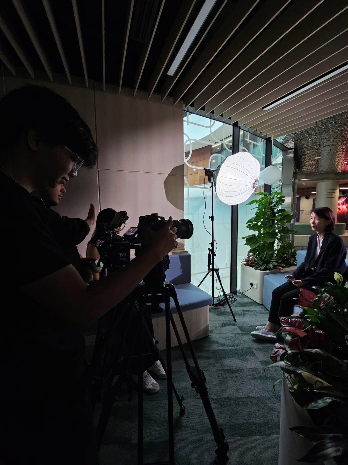 Camera crew filming a seated interview lit by a lantern softbox