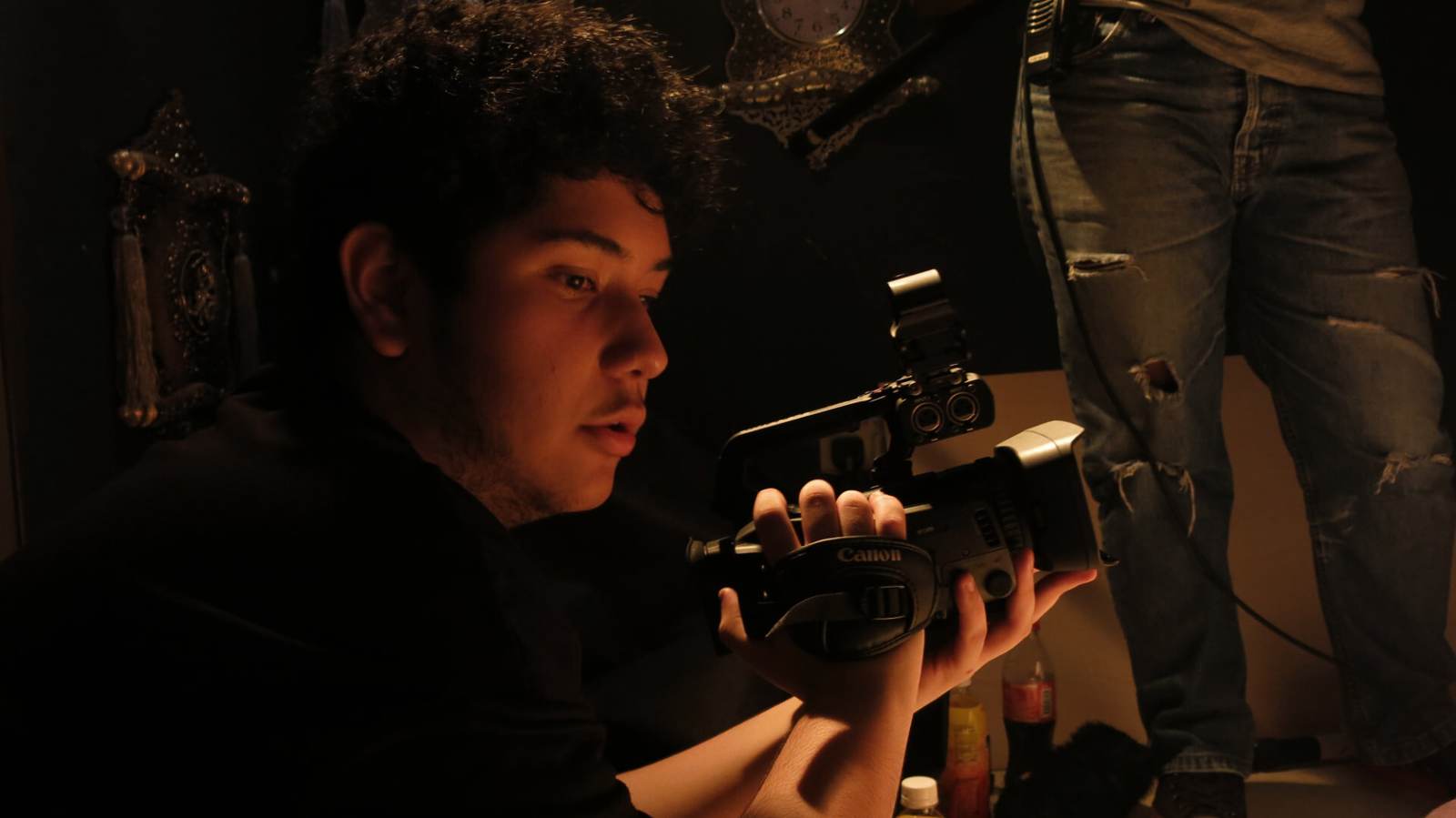 Camera operator checking framing on a handheld camcorder in warm practical light